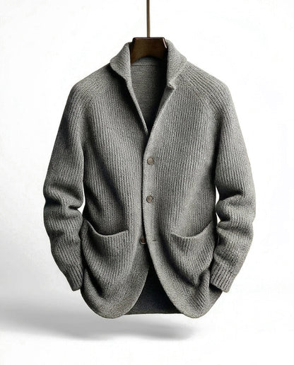 Graue Strickjacke mit Raglanärmeln, Knopfleiste und Schalkragen, frontal am Holzbügel aufgehängt. 4
