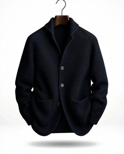 Dunkelblaue Strickjacke mit Schalkragen, drei Knöpfen und Taschen, frontal am Bügel vor hellem Hintergrund. 3
