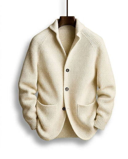 Cremeweiße Strickjacke mit grobem Rippmuster, Schalkragen und zwei aufgesetzten Taschen, frontal am Bügel. 5