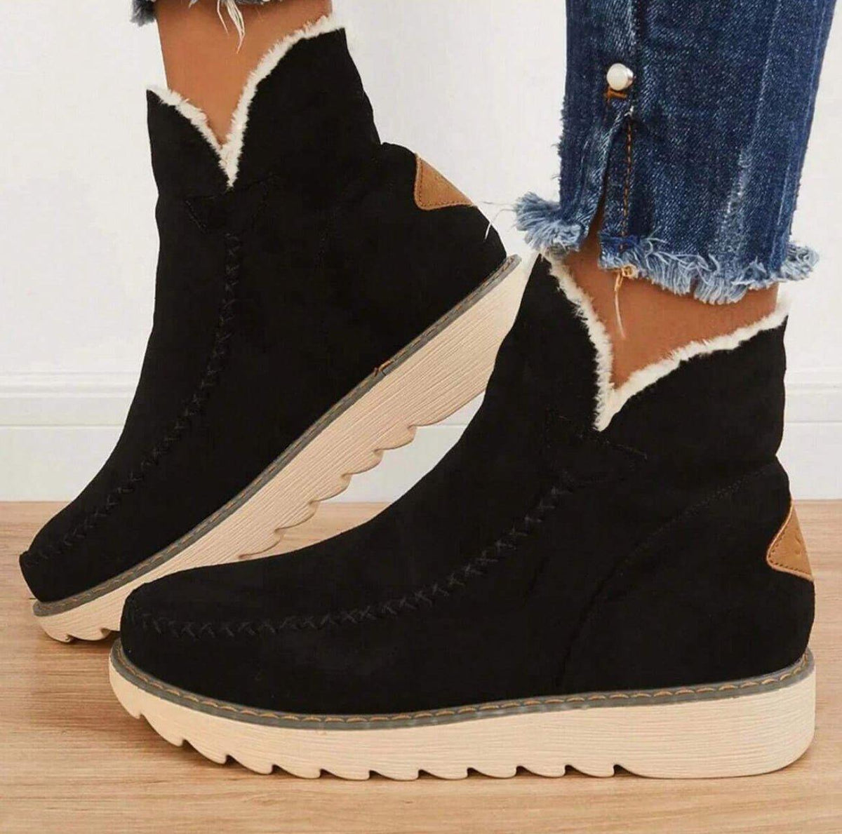 Schwarze Damen-Stiefeletten mit cremefarbenem Plüschrand und heller Profilsohle, seitlich getragen zu Jeans.