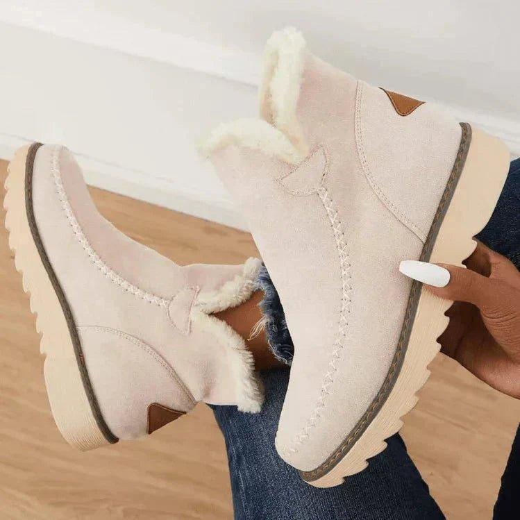 Beige Damen-Stiefeletten mit Plüschfutter, Ziernaht und gewellter Profilsohle, von einer Hand gehalten.