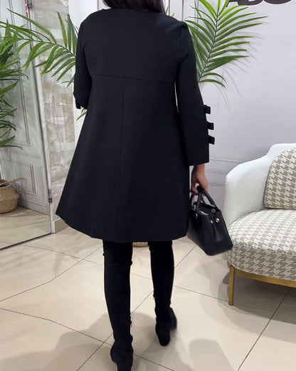 Frau in schwarzem Mantel, schwarze Hose, schwarze Tasche, moderne Inneneinrichtung.