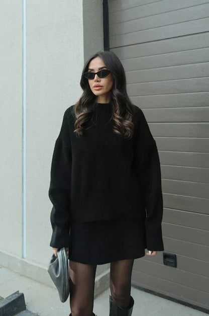 Model in schwarzem Strick-Zweiteiler mit langem, weitem Pullover und kurzem Rock, dazu Strumpfhose und schwarze Stiefel. 5