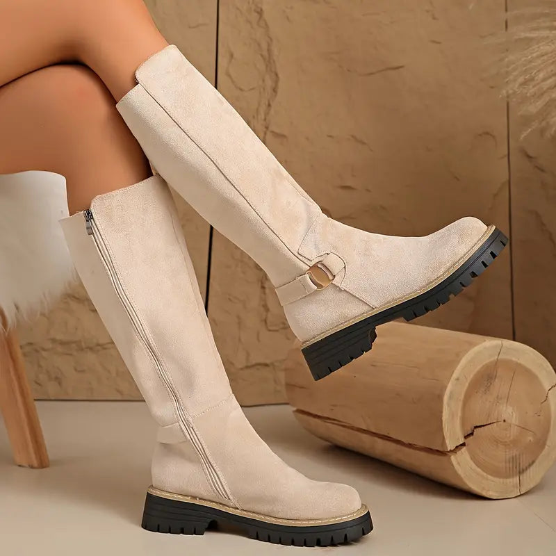 Beigefarbene kniehohe Stiefel mit Reißverschluss an der Innenseite, goldfarbener Schnalle und schwarzer Sohle.