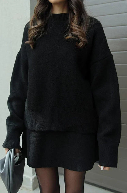 Detailansicht des schwarzen Strickpullovers mit weiten Ärmeln und Rippbündchen sowie dem kurzen schwarzen Rock. 6