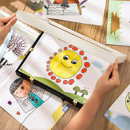 Hände legen eine Kinderzeichnung mit lächelnder Sonne in ein flaches Rahmenfach auf einem Holztisch.