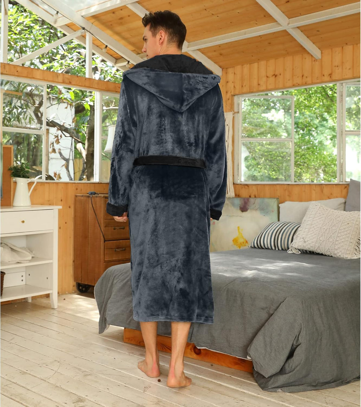 Mann im grauen Fleece-Bademantel mit Kapuze im Schlafzimmer, gemütliche Morgenroutine.