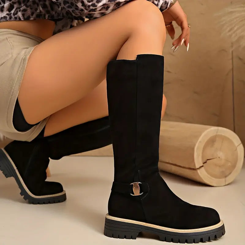 Schwarze Stiefel mit hohem Schaft und Schnalle, im Detail an einem Model mit beigen Shorts.