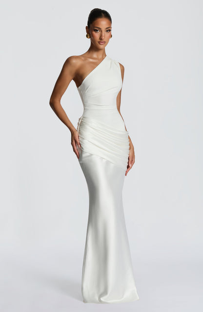 Seitliche Dreiviertelansicht des cremeweißen One-Shoulder-Kleides mit Raffung an der Hüfte und fließendem, bodenlangem Satinrock. 22