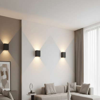 Drei schwarze, würfelförmige Wandlampen strahlen Licht nach oben und unten und zeichnen helle Dreiecke auf eine Wand im Wohnzimmer. 1