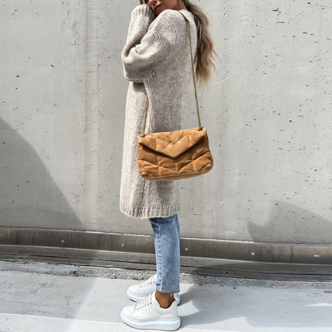 Frau in beigem Strickpullover, blauer Jeans, weißen Sneakers, brauner Umhängetasche.