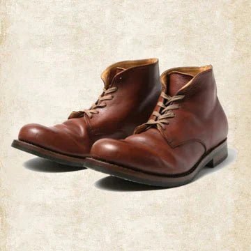 Paar braune Lederschnürstiefel in Schrägansicht von vorn auf hellem, strukturiertem Hintergrund, mit hellen Schnürsenkeln und flacher Absatzsohle. 1