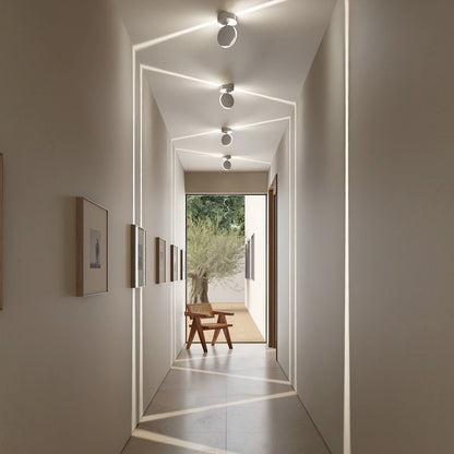 Flur mit vier Deckenleuchten, deren gedrehte Köpfe schräge Lichtlinien über Decke, Wände und Boden werfen. 6