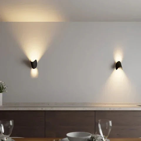 Zwei schwarze Wandleuchten an heller Wand über einem Sideboard mit Licht nach oben und unten.