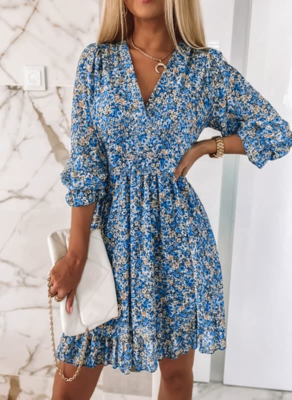 Frau in blauem Blumenkleid mit weißer Handtasche vor Marmortapete.
