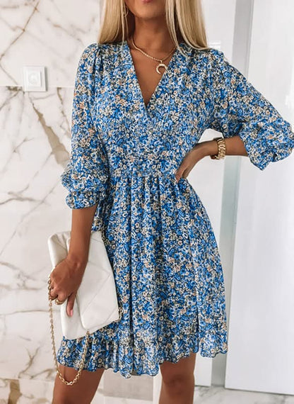 Frau in blauem Blumenkleid mit weißer Handtasche vor Marmortapete.