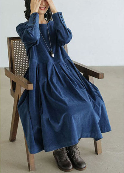 Frau in blauem Jeanskleid mit Taschen, Knöpfen, Herbstmode, sitzt auf Holzstuhl.