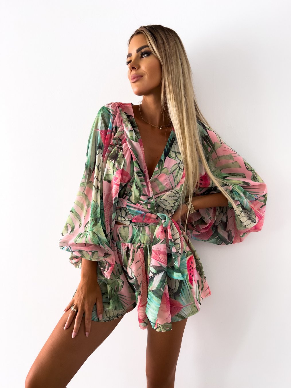 Frau in grün-rosa geblümtem Sommerkleid, V-Ausschnitt, lange Ärmel, tropisches Design.