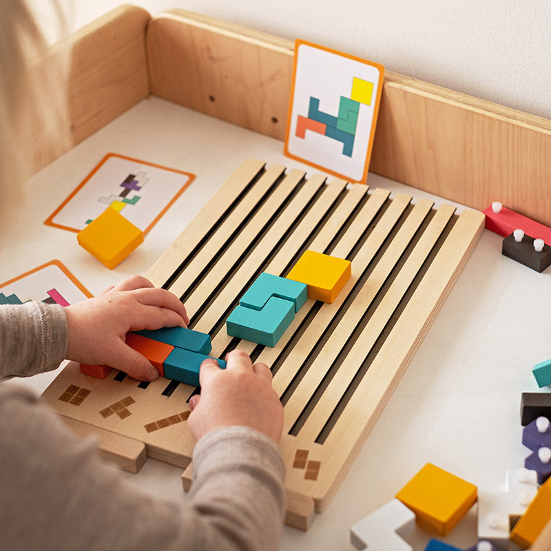 Holz-Tetris-Puzzlespiel mit Kind beim Einlegen farbiger Steine ins Holzbrett, Detail.