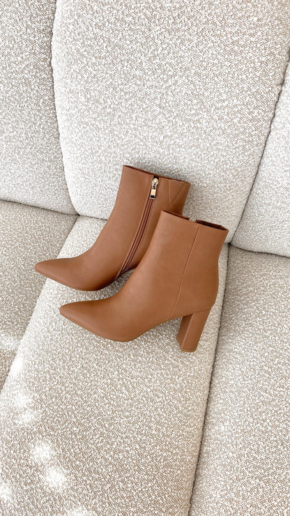 Braune Damen-Stiefeletten aus Leder mit Reißverschluss auf beigem Sofa.