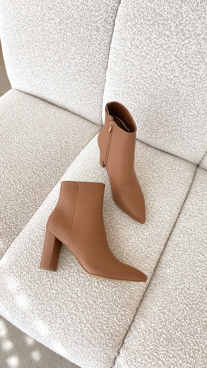 Braune Damen-Stiefeletten aus Leder mit Blockabsatz auf beigem Sofa, modisch und elegant.