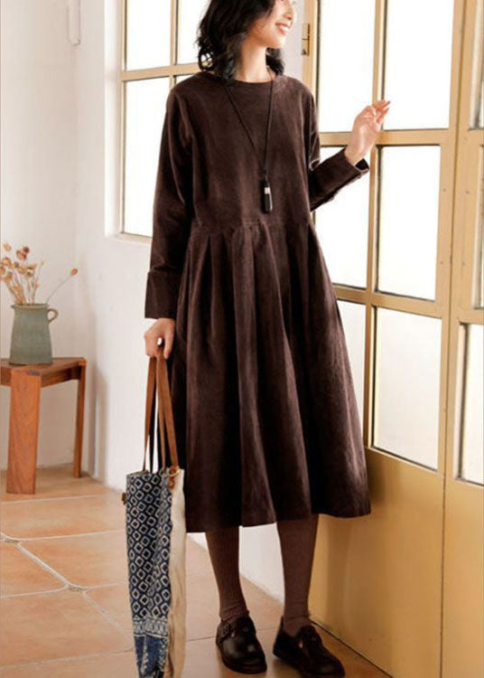 Frau in braunem Herbstkleid mit langen Ärmeln, trägt Tasche, steht vor Fenster.
