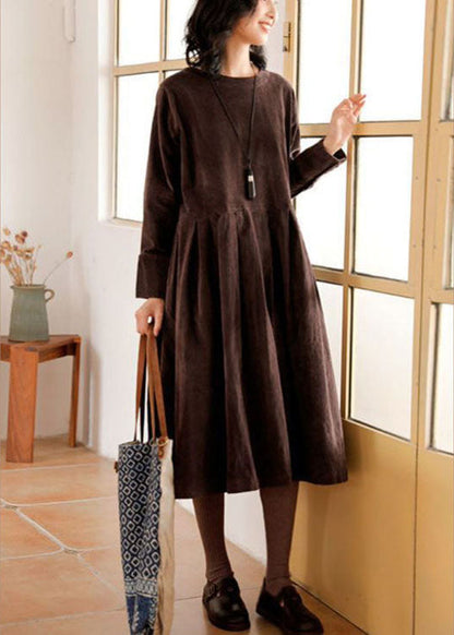 Frau in braunem Herbstkleid mit langen Ärmeln, trägt Tasche, steht vor Fenster.