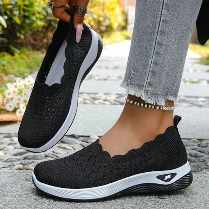 Schwarze Strick-Slipper, ein Schuh am Fuß, der andere angehoben, weiße Mittelsohle 13