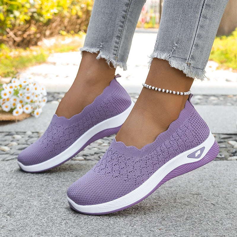Lilafarbene Strick-Slipper mit weißer Sohle, getragen zur Jeans auf einem Steinweg 19