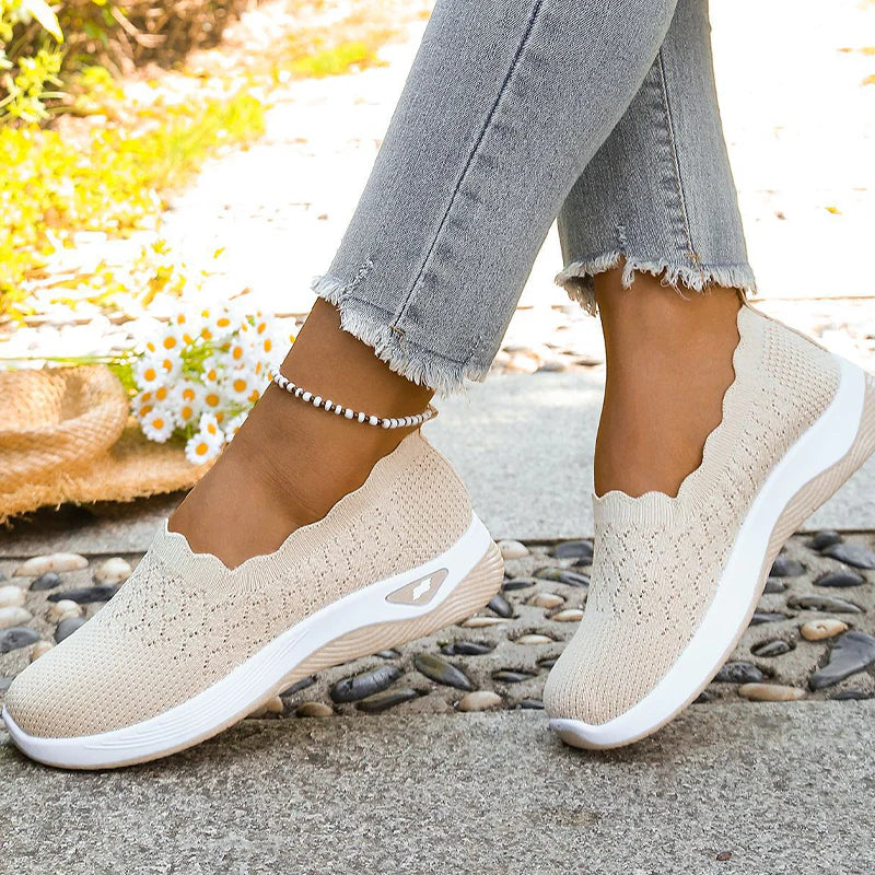 Beige Slipper an den Füßen einer Frau, Seitenansicht mit Sohlendetail und Gänseblümchen im Hintergrund 8