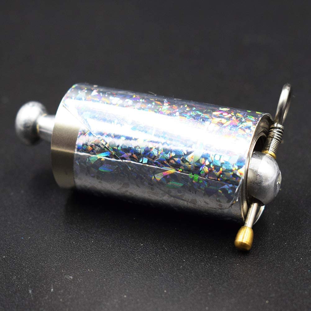 Nahaufnahme der Rolle mit holografischer Folie, Metallknauf, Feder, Ring und Messingknopf auf dunklem Untergrund 5