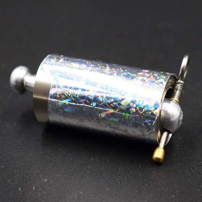 Nahaufnahme der Rolle mit holografischer Folie, Metallknauf, Feder, Ring und Messingknopf auf dunklem Untergrund 5