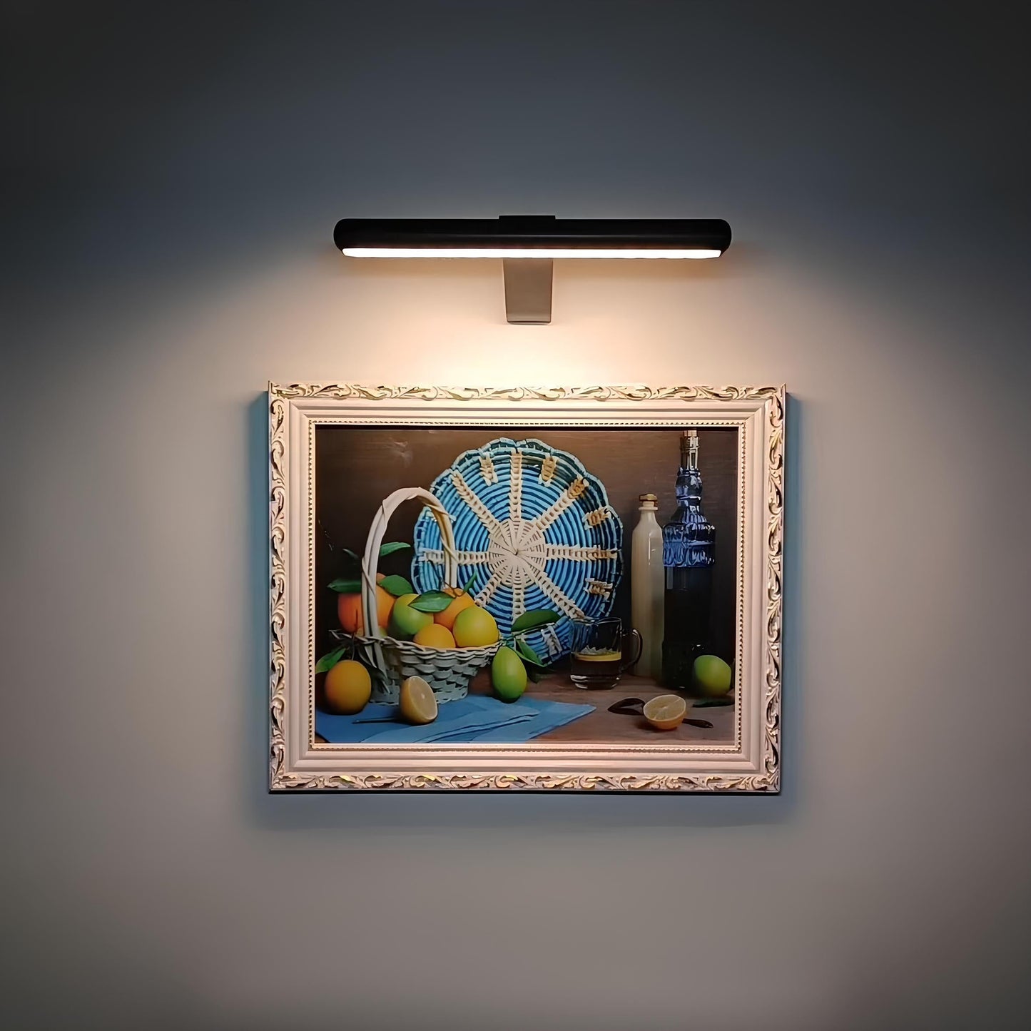 Gemälde mit Obstkorb, Zitronen, Flasche und blauem Fächer, beleuchtet, im dekorativen Rahmen.