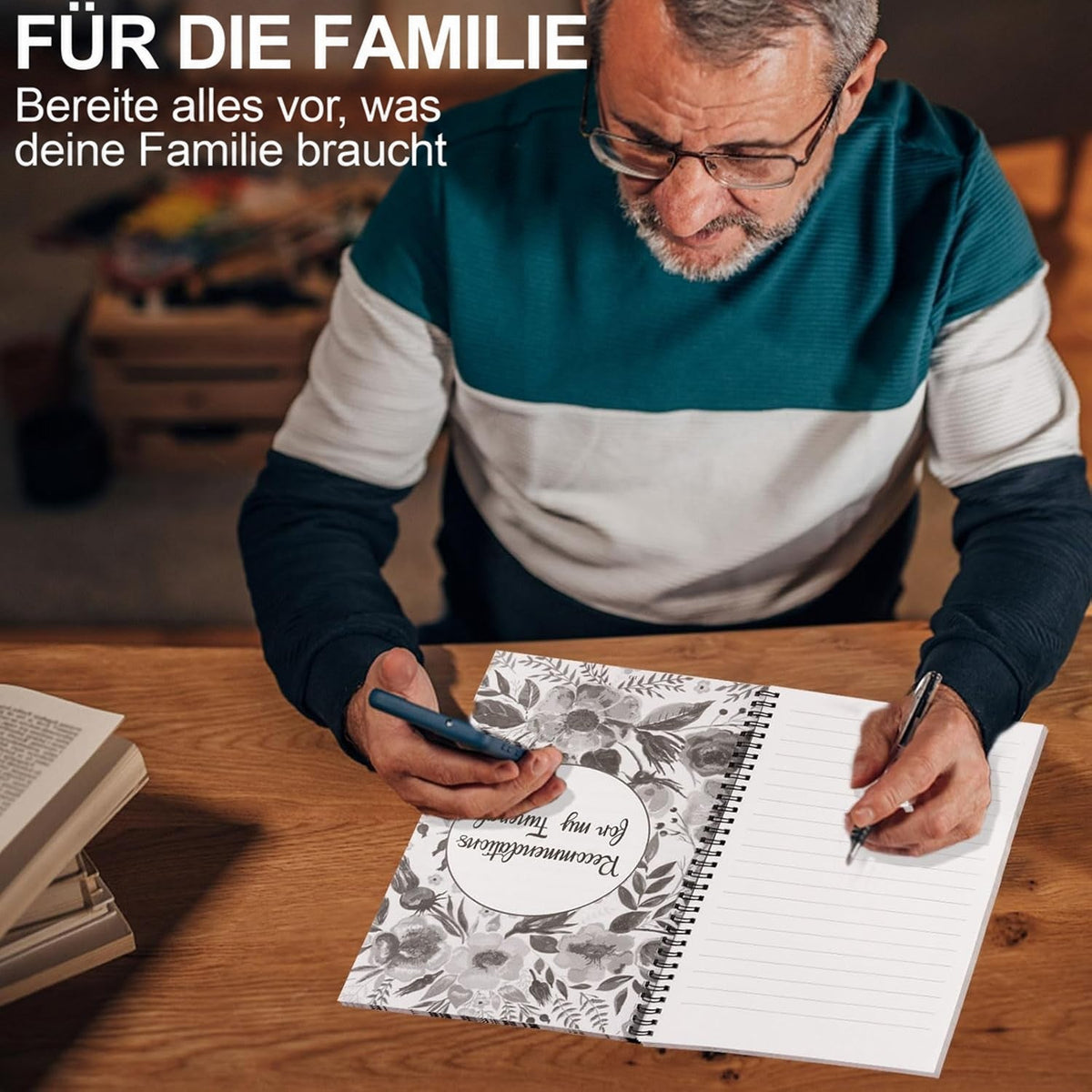 Älterer Mann mit Brille am Holztisch, schreibt mit Stift in den aufgeschlagenen Planer und hält ein Smartphone in der Hand. 4