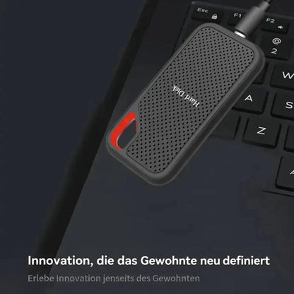 Schwarze SSD mit rotem Detail liegt per Kabel verbunden auf einer Laptop-Tastatur 2