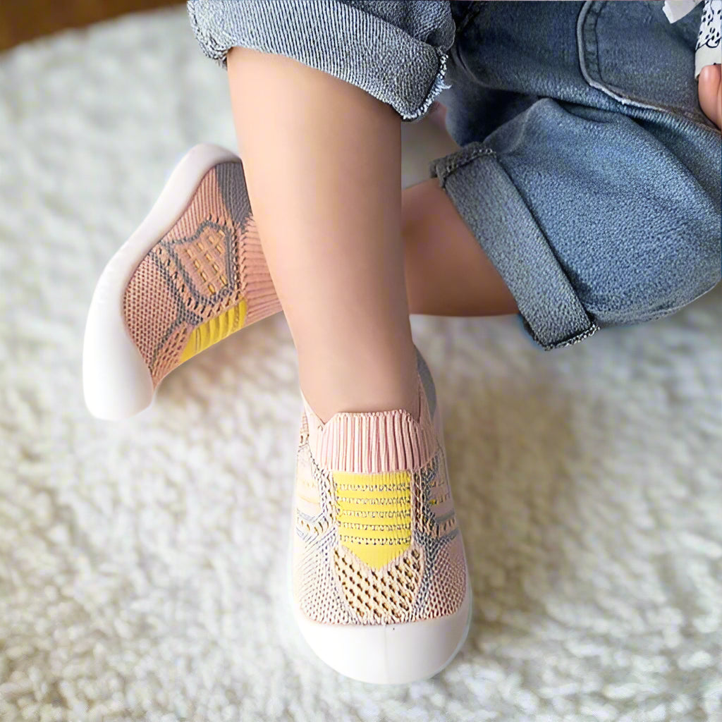 Rosa Babyschuhe aus Netzstrick mit gelbem Streifen an Kinderfüßen, another view
