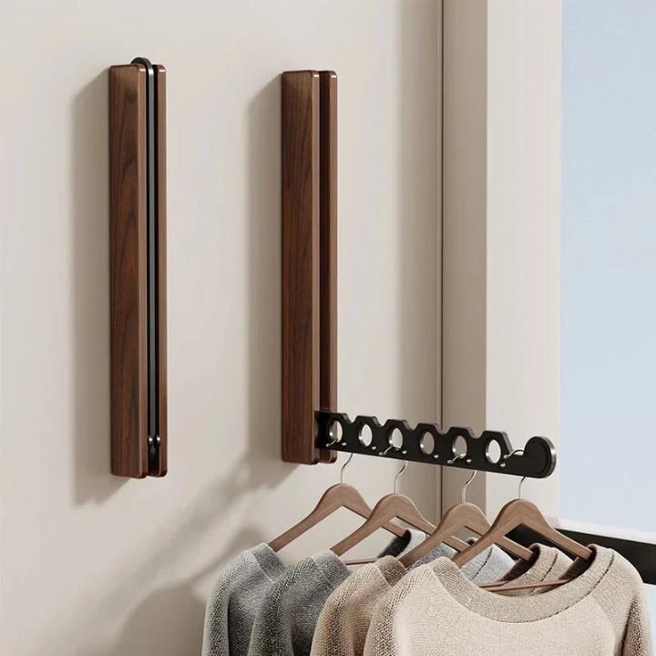Zwei dunkle Holz-Wandhaken, einer eingeklappt und einer ausgeklappt, am schwarzen Arm hängen Pullover an Holzbügeln. 7