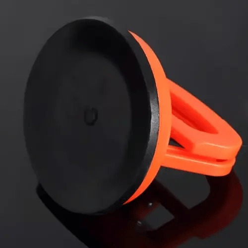 Unterseite eines orangefarbenen Dellenabziehers mit schwarzer Gummi-Saugfläche auf dunkler, glänzender Fläche.