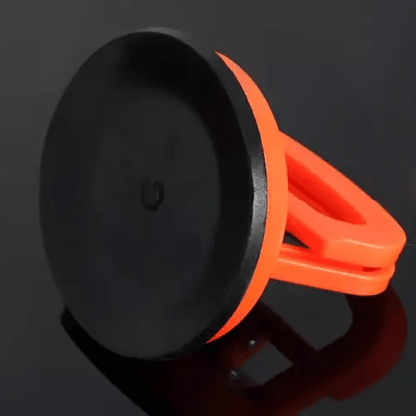 Unterseite eines orangefarbenen Dellenabziehers mit schwarzer Gummi-Saugfläche auf dunkler, glänzender Fläche.
