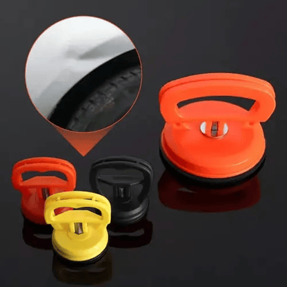 Drei Saugnapf-Dellenabzieher in Orange, Gelb und Schwarz mit Nahaufnahme einer kleinen Delle am Autokotflügel.