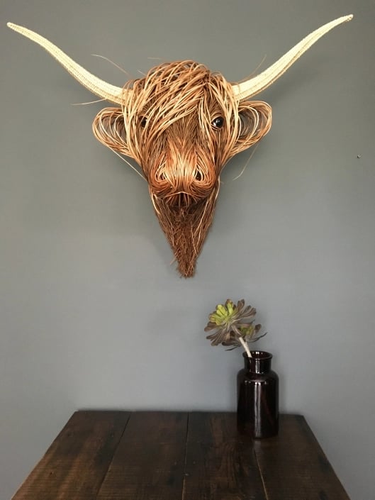 Kuhkopf mit weit ausladenden Hörnern an grauer Wand über einem Holztisch mit Vase 6