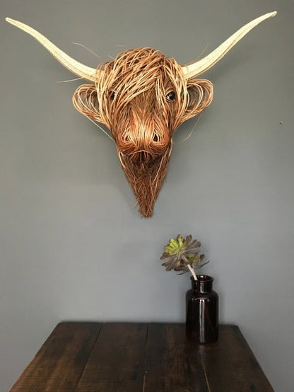 Kuhkopf mit weit ausladenden Hörnern an grauer Wand über einem Holztisch mit Vase 6