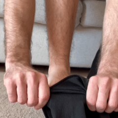 Nahaufnahme: Zwei Hände halten den Bund eines dunklen Kleidungsstücks am Unterschenkel vor einem Sofa 5