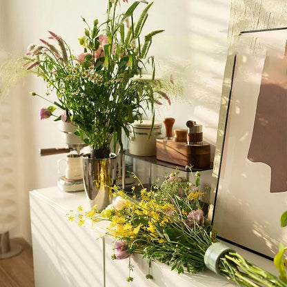 Wildblumenstrauß in einer Metallvase auf einer weißen Kommode, daneben liegt ein gelb-rosa Strauß mit grünem Einsatz an den Stielen. 3