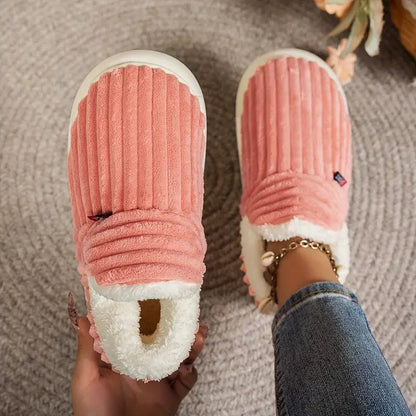 Korallrosa gerippte Hausschuhe von oben, ein Schuh in der Hand gehalten, der andere am Fuß.