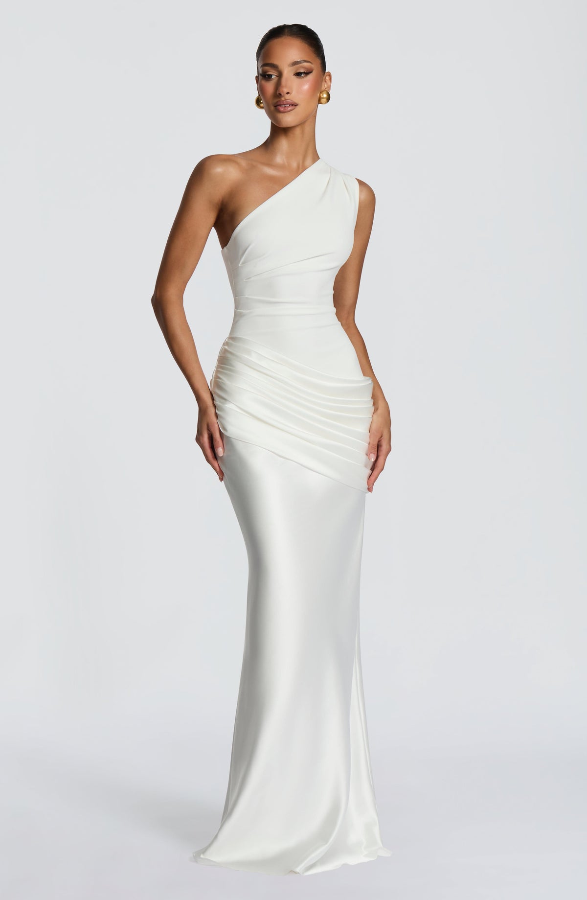 Frau in cremeweißem asymmetrischem Maxikleid mit gerafftem Satinrock, leicht seitlich fotografiert, Hand an der Hüfte, goldene Kugelohrringe. 21