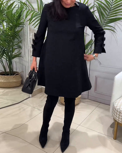 Frau in schwarzem Kleid mit Tasche, schwarze Stiefel, elegante Mode, Innenraum, Pflanzen im Hintergrund.