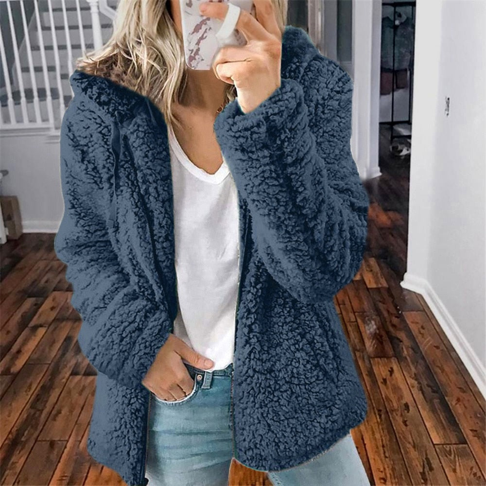 Frau in blauer Teddyfelljacke, weißem T-Shirt und Jeans im Innenraum.