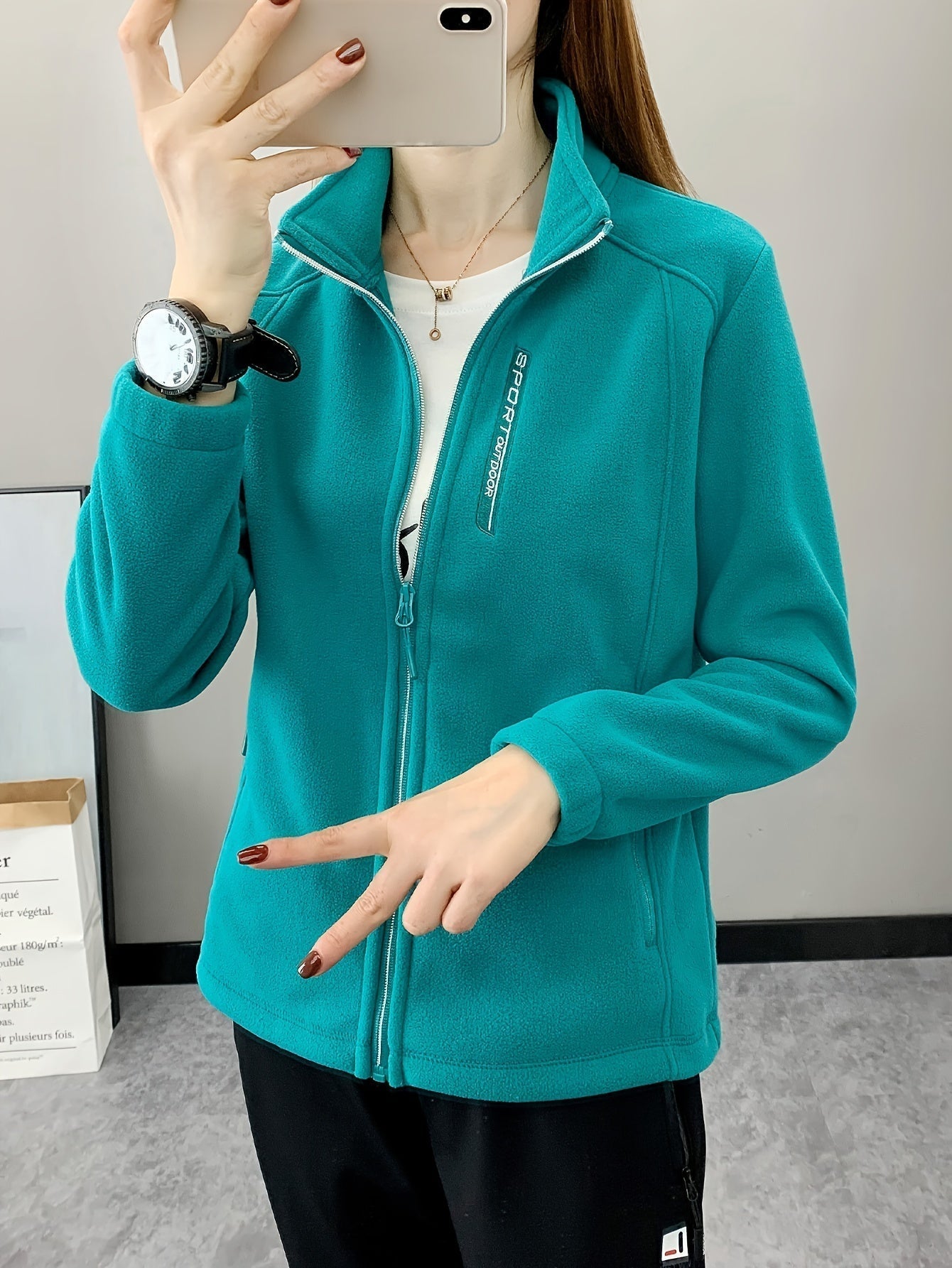 Frau in türkisfarbener Fleecejacke mit Reißverschluss, Sportuhr, Smartphone, lässiger Stil.