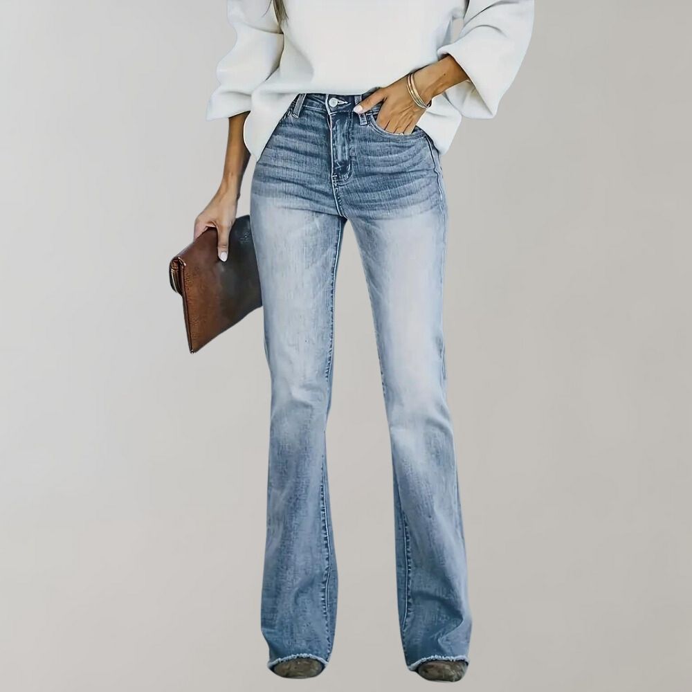 Frau in blauer Schlagjeans und weißem Pullover, hält braune Clutch.
